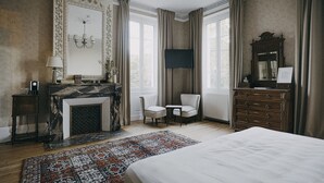 Une chambre à coucher avec un grand lit, une cheminée, une télévision, une commode et un fauteuil.