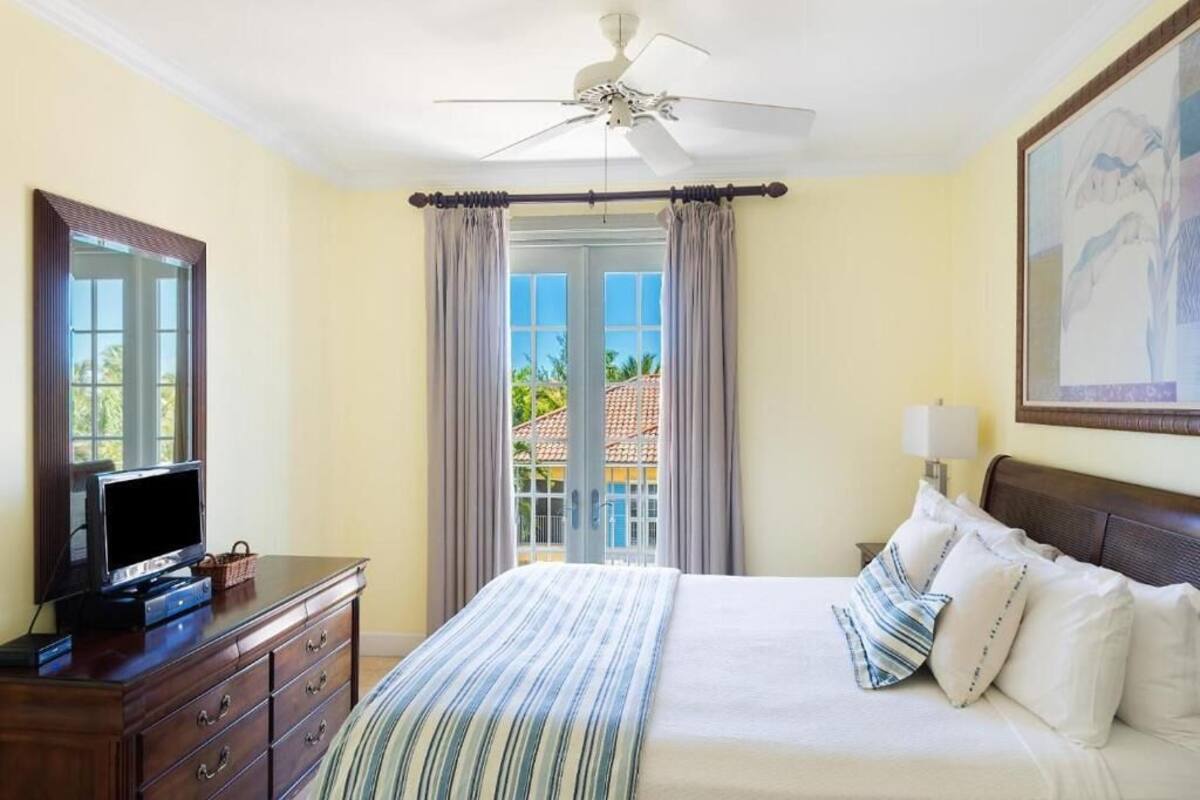A hotel room with a bed, a TV on a dresser, a ceiling fan, and a view of the outside.