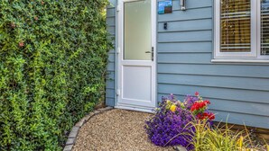 A house with a white door, a small window with blinds, and a garden with colorful flowers. - Charming Chalet A Stone's Throw From The Beach! - Pass the Keys (Chichester)