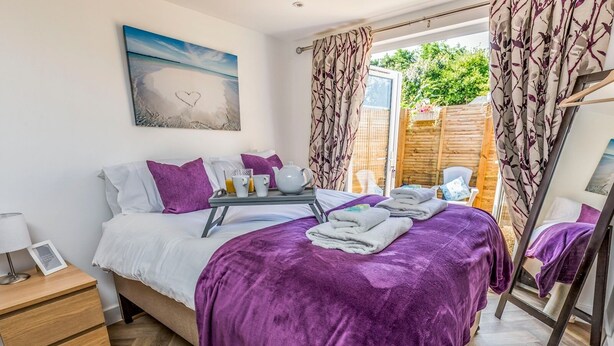 A bedroom with a bed, bedside table, and a window with curtains. - Charming Chalet A Stone's Throw From The Beach! - Pass the Keys (Chichester)