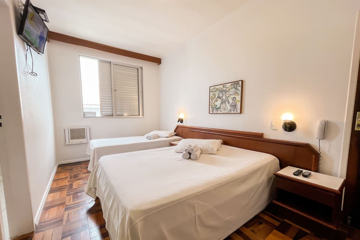 Habitación de hotel con dos camas, piso de madera, televisor montado en la pared y un cuadro en la pared.