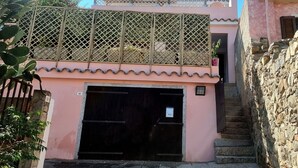 Un bâtiment à la façade rose, avec une porte de garage noire et un escalier menant à un deuxième étage doté d’un balcon en treillis.