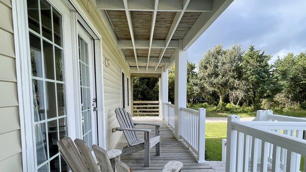 A wooden deck with two Adirondack chairs and a white railing.