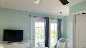 A bedroom with a bed, a television, a chair, and a window with curtains.