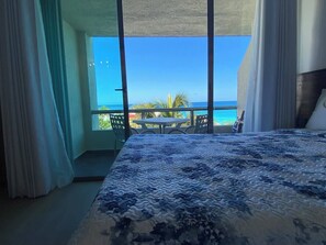 A hotel room with a large bed, a balcony with a view of the ocean, and a table and chairs outside.