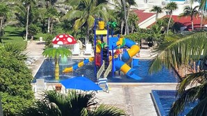 Vandland med rutsjebaner og en pool, omgivet af palmer og udsigt til havet.