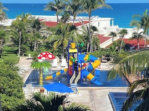 A water park with slides and a pool, surrounded by palm trees and a view of the ocean.