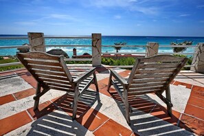 Two wooden chairs facing a beach with a clear view of the ocean.