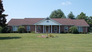 A two-story brick house with a front porch, a well-maintained lawn, and a small garden with a birdbath. - Quiet-Country and Spacious Grandma's Duplex (Stamping Ground)