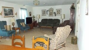 A living room with a blue sofa, a patterned armchair, a wooden dining table, and a television. - Quiet-Country and Spacious Grandma's Duplex (Stamping Ground)