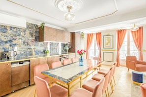 A modern kitchen with a marble countertop, a dining area with pink chairs, and a large window with orange curtains. - Merveil - Luxury Suite - Louvre - Aboukir VII (Paris)
