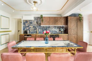 A modern kitchen with marble countertops, a central island, and pink chairs around a marble dining table. - Merveil - Luxury Suite - Louvre - Aboukir VII (Paris)