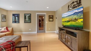 Una sala de estar con un televisor de pantalla plana grande, un sofá de cuero, una manta a cuadros y cuadros enmarcados en la pared.