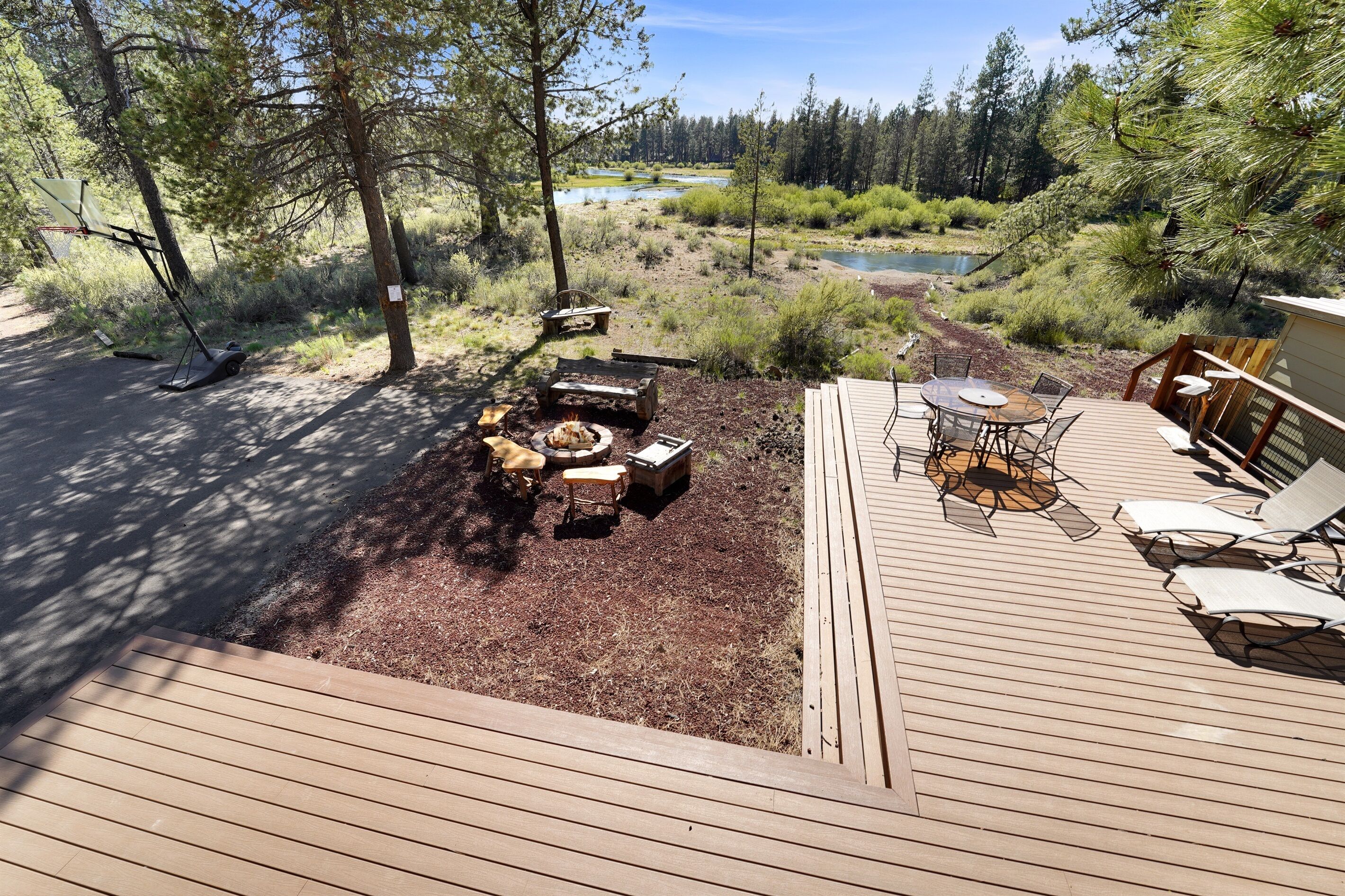 Um deck com móveis de exterior, uma lareira e vista para um lago rodeado por árvores.