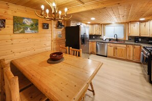 A wooden interior with a dining table, chairs, a refrigerator, a sink, and wooden cabinets.