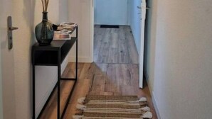 Un pasillo con piso de madera, una consola negra con un florero y una lámpara colgante.