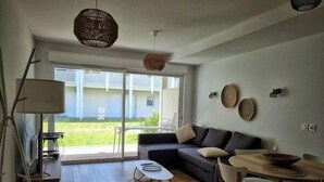 Una sala de estar moderna con un sofá, una mesa de comedor y sillas. Hay un ventanal con vista a un edificio blanco y una zona verde.