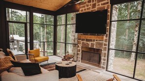 Ein gemütliches Wohnzimmer mit Kamin aus Stein, großen Fenstern und bequemen Sitzgelegenheiten.