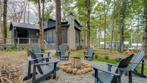 Eine Holzhütte mit Steinaußenwand, umgeben von Bäumen, mit Sitzgelegenheiten im Freien, Adirondack-Stühlen und einem Feuerkorb.