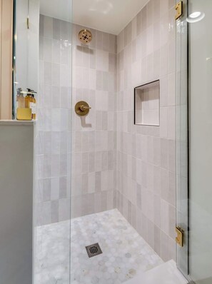 A modern shower with glass doors, a gold shower head, and a hexagonal tile floor.