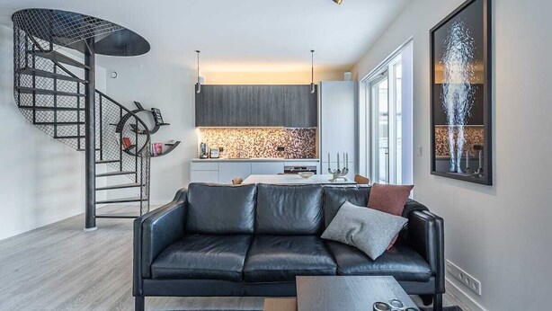 Ein modernes Wohnzimmer mit einem schwarzen Ledersofa, einem Couchtisch und einer Wendeltreppe.