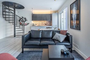 A modern living room with a black leather sofa, a coffee table, and a spiral staircase. - Luxury 2 BR apt w. rooftop area + indoor parking.  Best possible location. (Reykjavík)