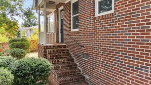 A brick house with a porch and steps leading to the front door. - 3BR Near Swamp Rabbit Trail • Fenced Yard • Pet-Friendly • 7 Min to Downtown (Greenville)