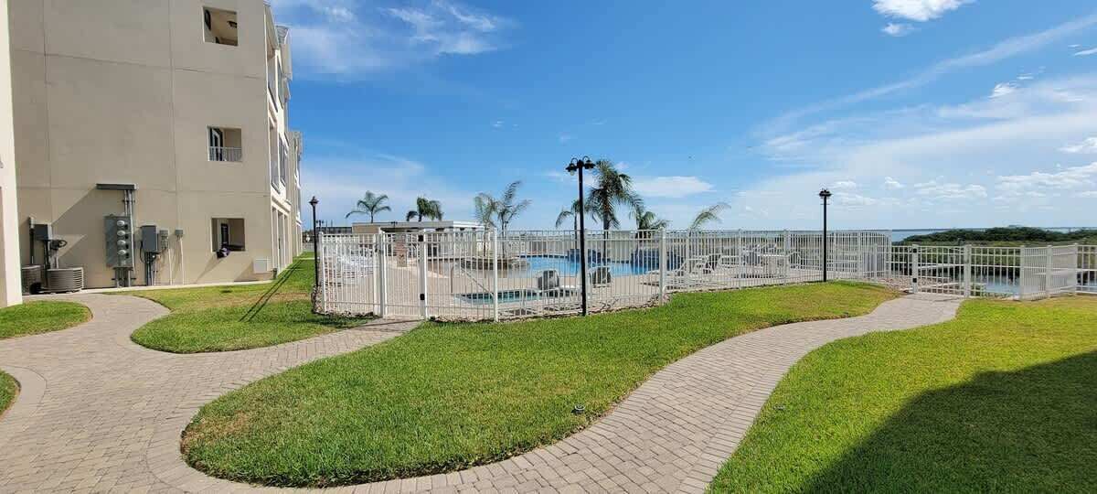 Un área de piscina con piscina cercada, un edificio con varias ventanas y cielo despejado.