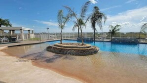 A swimming pool with a circular island, palm trees, and a fenced area. - 3 Level Luxury Beachlike Pool - Killer Sunsets (South Padre Island)