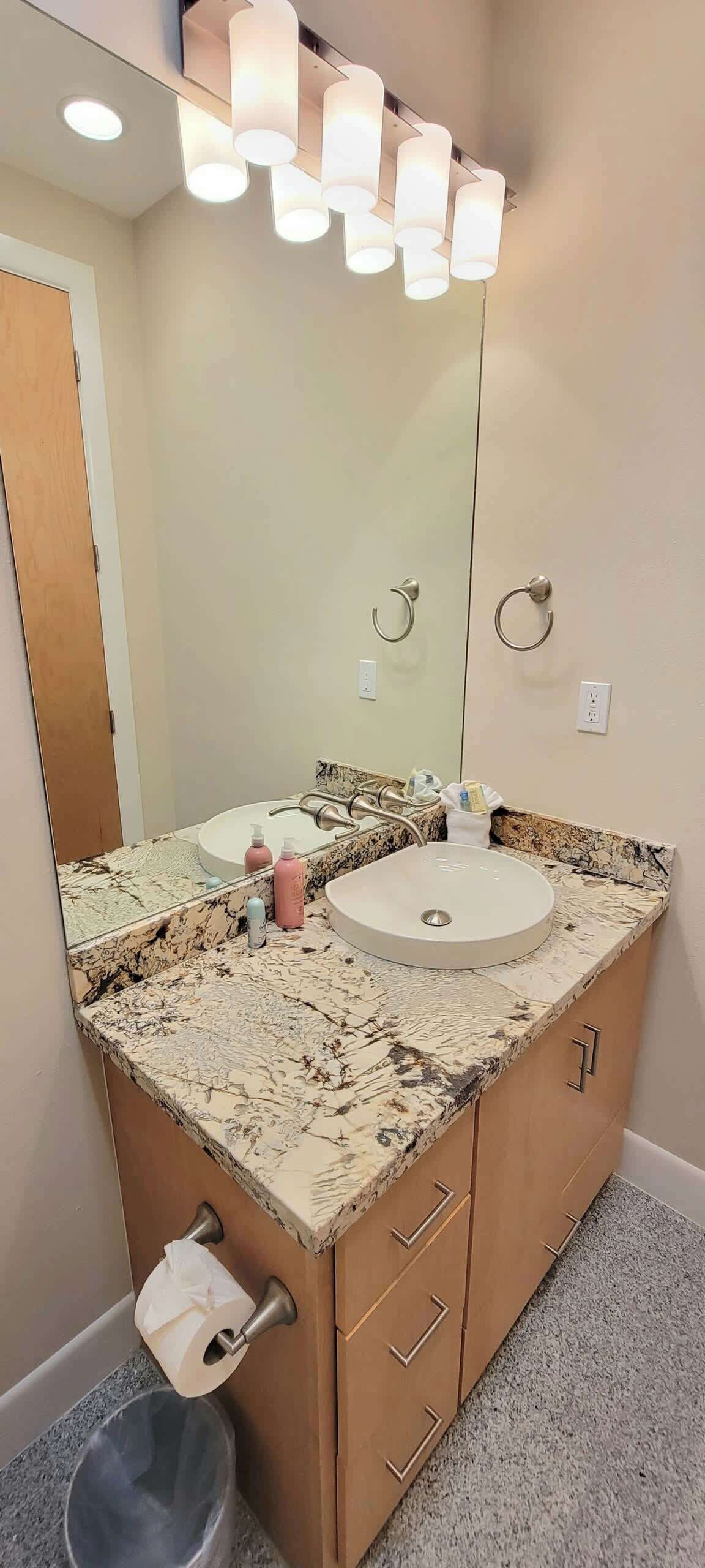 A bathroom with a marble countertop, two sinks, a large mirror, and a toilet paper holder.