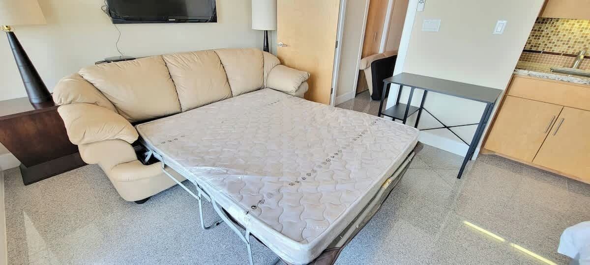 Una habitación compacta con sofá cama, una mesita y un televisor montado en la pared.