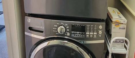 A stacked washer and dryer unit with control panels and a small shelf with detergent boxes.