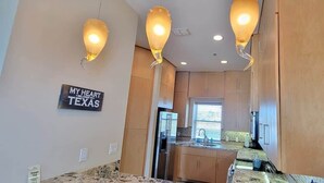 A modern kitchen with wooden cabinets, a central island, and pendant lighting. A sign on the wall reads "MY HEART IS IN TEXAS". - 3 Level Luxury Beachlike Pool - Killer Sunsets (South Padre Island)
