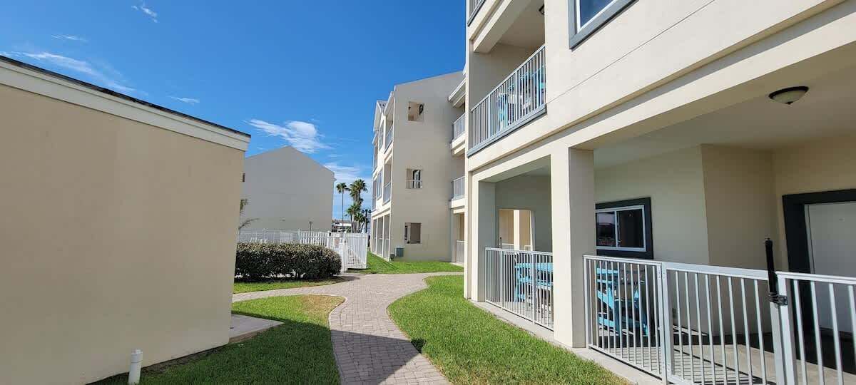 Um edifício residencial com um caminho pavimentado, um pequeno gramado e uma varanda com guarda-corpo.
