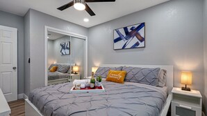 A bedroom with a bed, bedside tables, a ceiling fan, a mirror, and artwork on the wall. - 2BR Apt, 5 Min to Busch Gardens | Unit B, Sleeps 6, Remodeled, Tampa (Tampa)