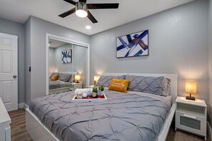Un dormitorio con cama, mesitas de noche, ventilador de techo, espejo y obras de arte en la pared.