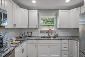 A modern kitchen with white cabinets, a granite countertop, and a window with a view of greenery.
