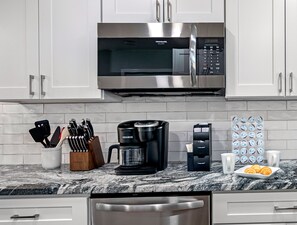 A kitchen with white cabinets, a stainless steel microwave, a coffee maker, and a coffee pod dispenser. - 2BR Apt, 5 Min to Busch Gardens | Unit B, Sleeps 6, Remodeled, Tampa (Tampa)