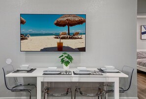 Un comedor con una mesa dispuesta para dos, una planta en maceta y un cuadro con una playa.