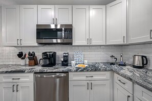 Una cocina moderna con armarios blancos, un microondas de acero inoxidable, una cafetera y un hervidor en la encimera.