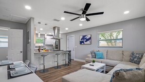 A modern living room with a sofa, coffee table, and a dining area with bar stools. - 2BR Apt, 5 Min to Busch Gardens | Unit B, Sleeps 6, Remodeled, Tampa (Tampa)