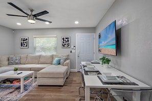 A modern living room with a sofa, coffee table, and a TV on a wall.