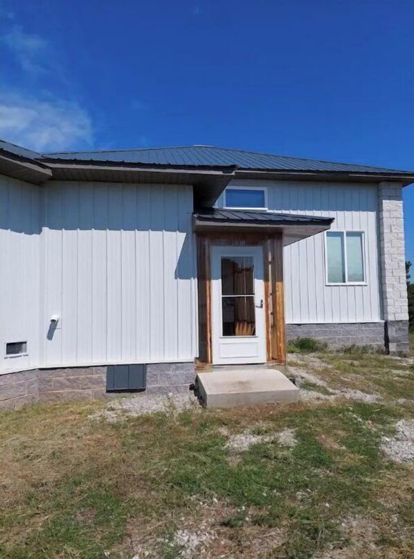 Situated on a grassy area, this single-story residence features a white exterior and a small porch with a wooden door.