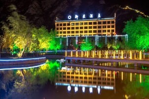 Un edificio con señalización iluminada, un cuerpo de agua reflectante al frente y follaje circundante.