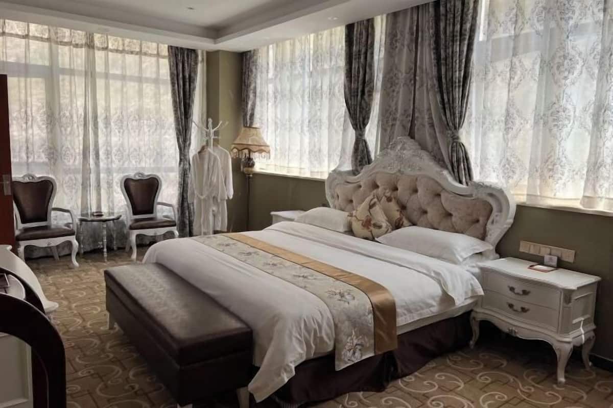 A hotel room with a large bed, a bedside table, a chair, and a lamp.