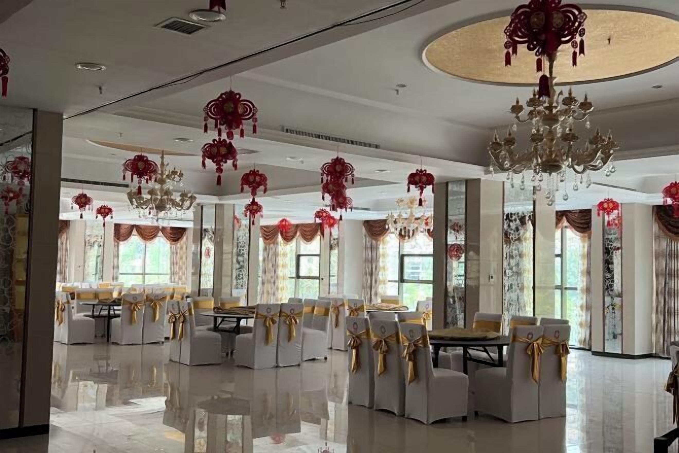 A spacious dining area with round tables and chairs, elegant chandeliers, and red hanging decorations.