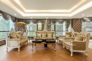 A luxurious living room with ornate furniture, large windows, and a tiled floor.