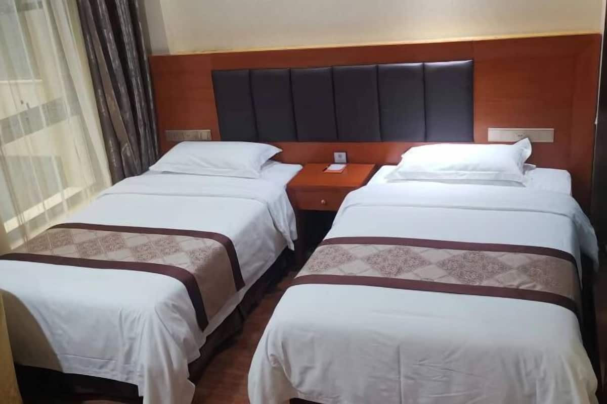 A hotel room with two single beds, a wooden headboard, and a nightstand between them.