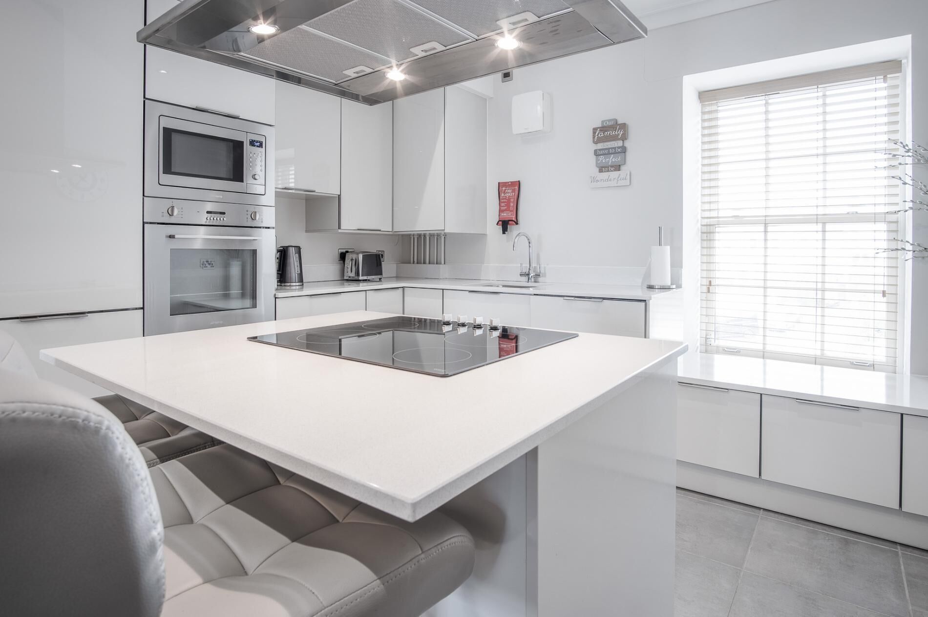A modern kitchen with white cabinetry, a built-in oven, a microwave, a coffee maker, and a large island with an induction cooktop.