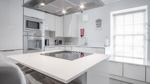 A modern kitchen with white cabinetry, a built-in oven, a microwave, a coffee maker, and a large island with an induction cooktop.
